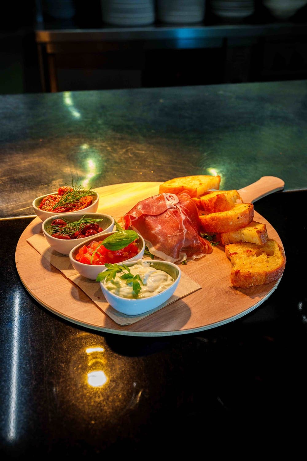 Antipasti-Brett mit Prosciutto, geröstetem Brot, Oliven, getrockneten Tomaten und Dip auf schwarzem Tresen