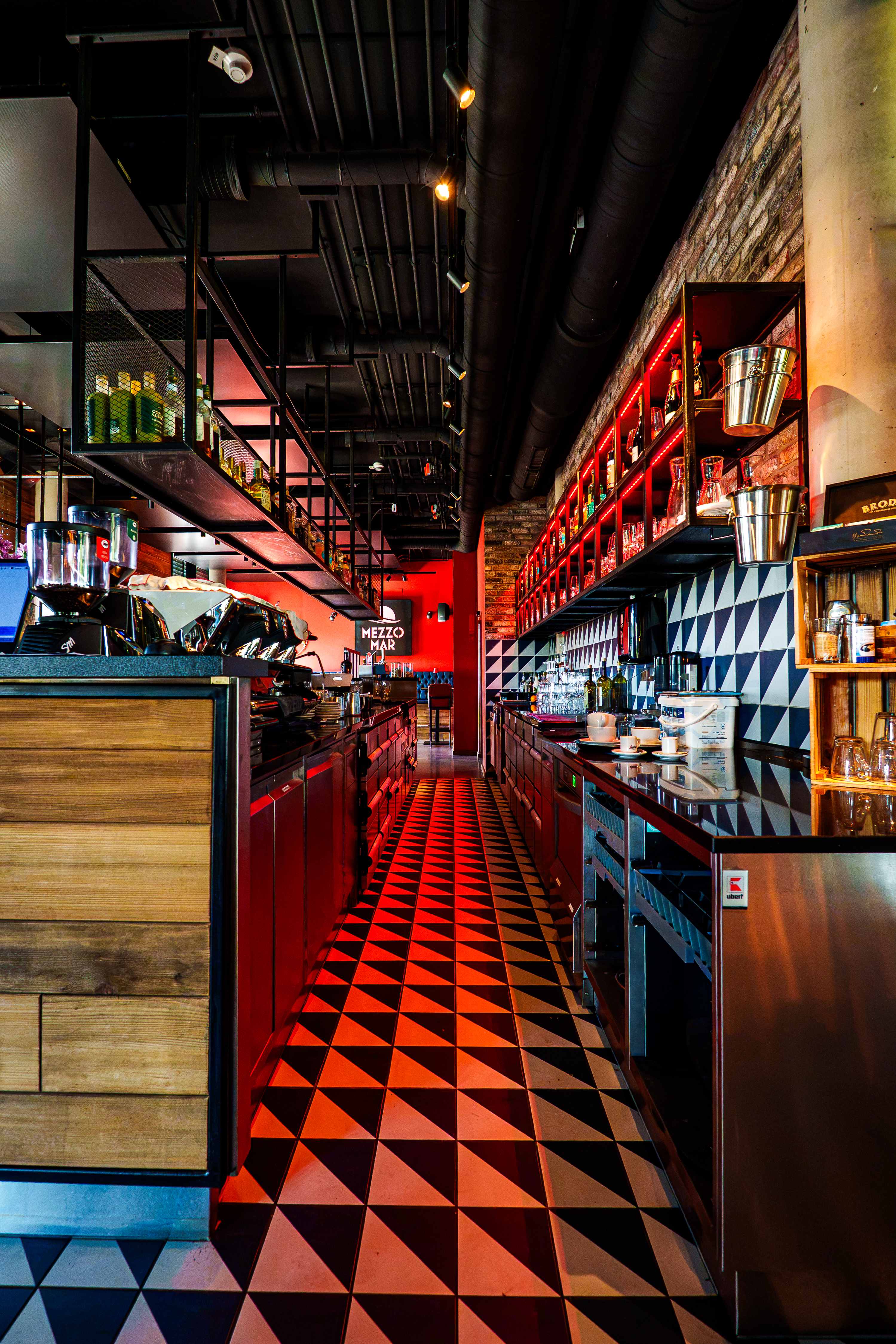 Bar im Mezzomar mit Espressomaschine, rot beleuchteten Regalen und schwarz-weißem Dreiecksboden