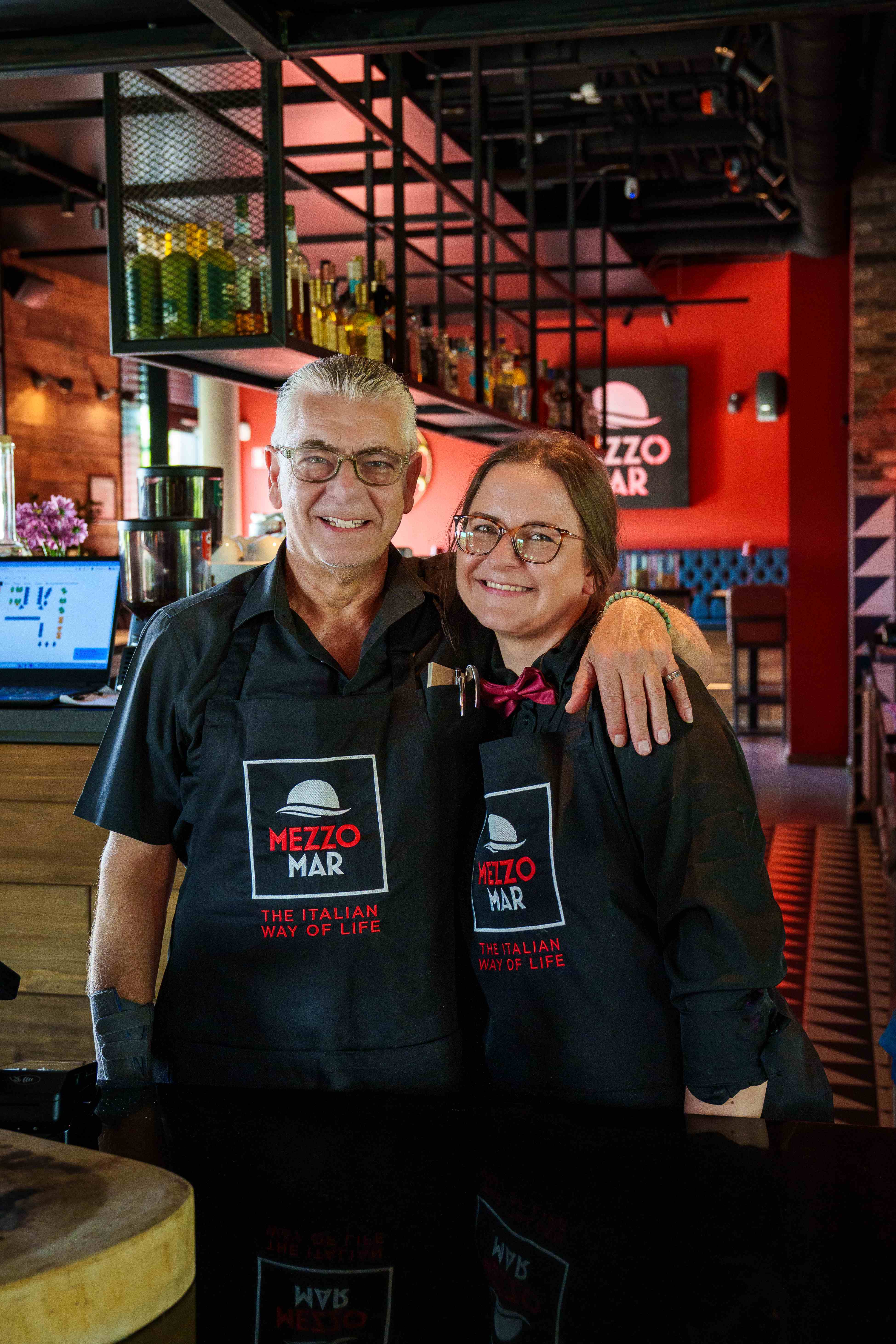 Zwei lächelnde Teammitglieder in schwarzen Mezzomar-Schürzen im Restaurant