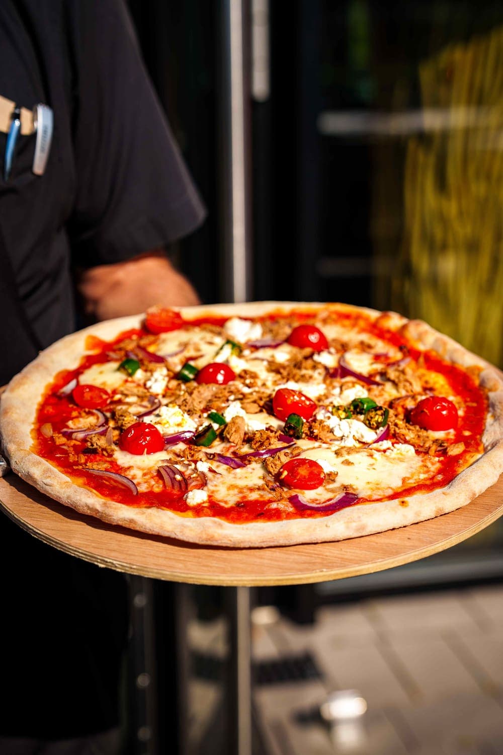 Frisch gebackene Pizza mit Thunfisch, Cherrytomaten und roten Zwiebeln auf einem Holzbrett